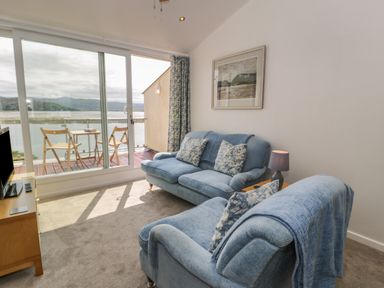 A living room with blue sofas and a TV next to a balcony with outdoor chairs at 25 South Snowdon Wharf in Porthmadog