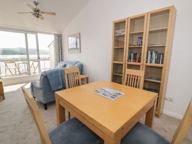 A dining area with a wooden table and chairs next to a blue sofa and a glass cabinet with books at 25 South Snowdon Wharf in Porthmadog