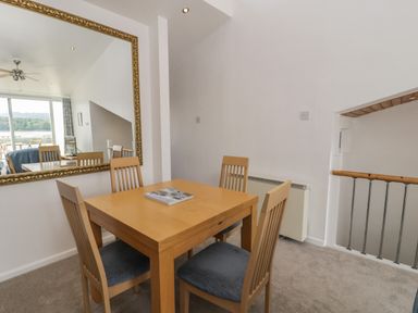 A dining area with a wooden table and four chairs next to a large mirror reflecting a living space at 25 South Snowdon Wharf in Porthmadog