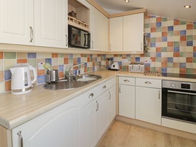 A kitchen with white cabinets a sink a microwave toaster kettle and blender at 25 South Snowdon Wharf in Porthmadog