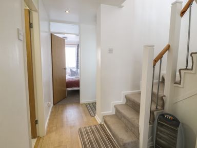 A hallway with carpeted stairs and a wooden floor next to an open door revealing a bedroom at 25 South Snowdon Wharf in Porthmadog