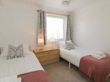 A bedroom with two single beds a wooden chest of drawers two table lamps and patterned curtains at 25 South Snowdon Wharf in Porthmadog