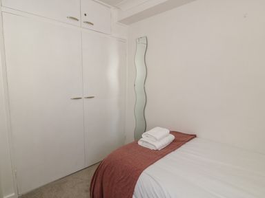 A bedroom with a bed covered with white sheets and a brown blanket with folded towels on top a built in white wardrobe and a tall wavy mirror on the wall at 25 South Snowdon Wharf in Porthmadog