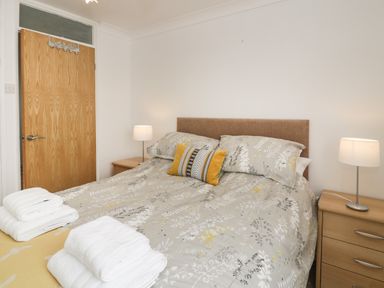 A bedroom with a double bed patterned bedding bedside tables with lamps and folded towels at 25 South Snowdon Wharf in Porthmadog