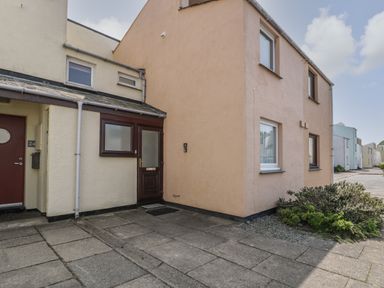 Exterior view of a two storey corner house with beige and light yellow walls next to a paved driveway with shrubs at 25 South Snowdon Wharf in Porthmadog