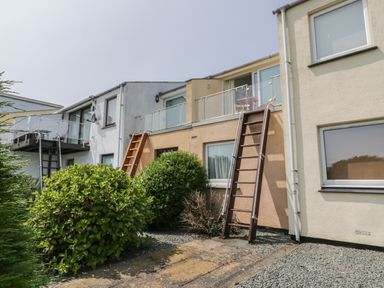 Exterior view of a residential building with stairs leading to glass balcony doors and bushes in front at 25 South Snowdon Wharf in Porthmadog