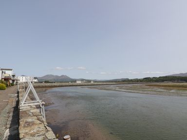A waterfront with a stone wall and buildings on the left and a body of water with mountains in the distance at 25 South Snowdon Wharf in Porthmadog