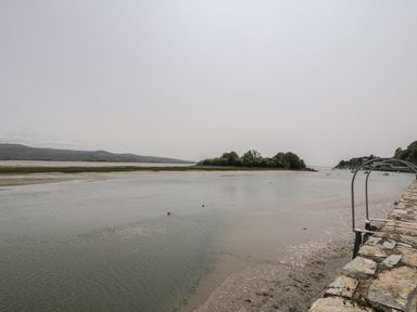 A river or estuary with a stone wall and metal ladder on the right surrounded by trees and hills at 25 South Snowdon Wharf in Porthmadog
