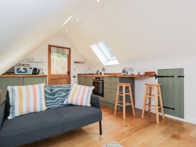 A kitchen area with green cabinets wooden countertops two wooden stools sofa with striped pillows and a wooden floor at The Rookery in Fulbrook near Burford