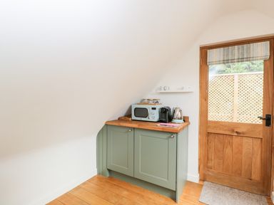 A corner kitchen area with a green cabinet wooden countertop microwave coffee machine electric kettle and wooden door at The Rookery in Fulbrook near Burford
