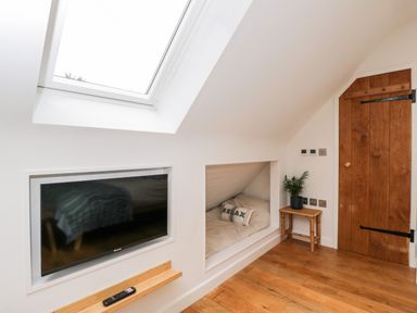 A bedroom with a wall-mounted TV a skylight a built-in bed nook with a relax pillow a wooden door and a small table with a plant at The Rookery Fulbrook near Burford