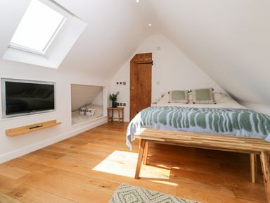 A bedroom with a bed pillows and bench under a slanted ceiling at The Rookery in Fulbrook near Burford