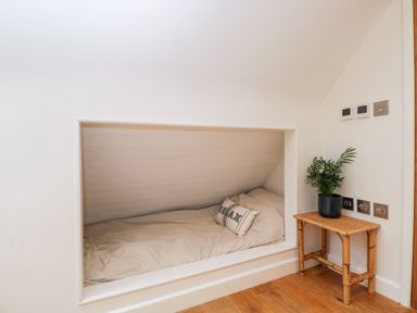 A built-in bed alcove with bedding and a pillow that says relax next to a small table with a plant at The Rookery in Fulbrook near Burford