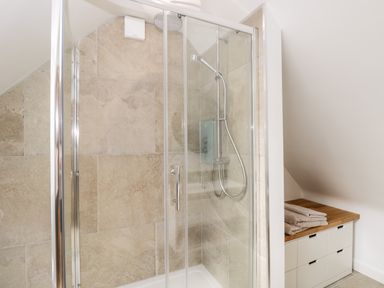 A bathroom with a glass enclosed shower and a wooden topped cabinet with folded towels at The Rookery Fulbrook near Burford