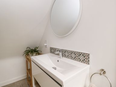 A bathroom sink with a round mirror above and patterned tiles behind at The Rookery in Fulbrook near Burford