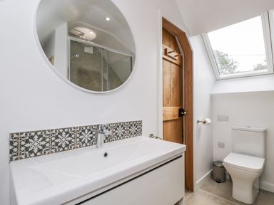 A bathroom with a sink and mirror a wooden door a toilet and a skylight window at The Rookery in Fulbrook near Burford
