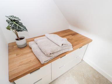 A wooden countertop with folded towels and a potted plant on white cabinets in a corner