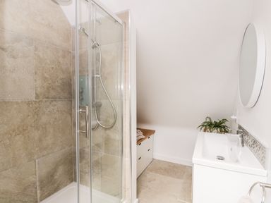 A bathroom with a glass shower enclosure a sink with a round mirror and a small plant at The Rookery in Fulbrook near Burford