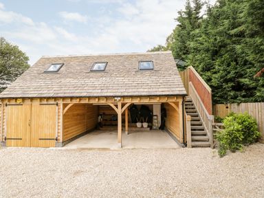 A wooden garage with two open bays and a closed door next to exterior stairs at The Rookery in Fulbrook near Burford