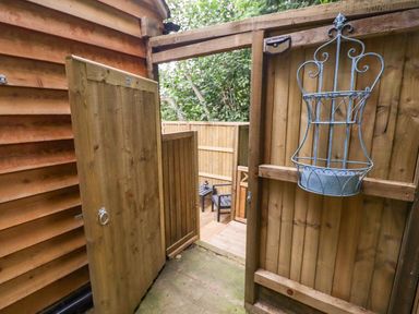 A wooden outdoor gate opening to a fenced patio with a chair and table at The Rookery in Fulbrook near Burford