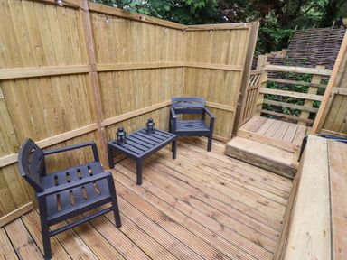 A small wooden deck area with two black chairs and a table with two lanterns at The Rookery in Fulbrook near Burford