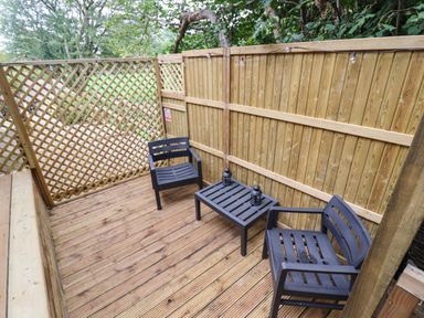 A wooden outdoor patio with two chairs a small table and string lights at The Rookery in Fulbrook near Burford