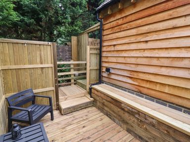 An outdoor wooden deck with a black chair and table next to a wooden building at The Rookery in Fulbrook near Burford
