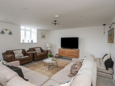 A living room with brown leather armchairs beige sectional sofa coffee table and a TV on a wooden stand at Ysgol Fawr Big School in Benllech