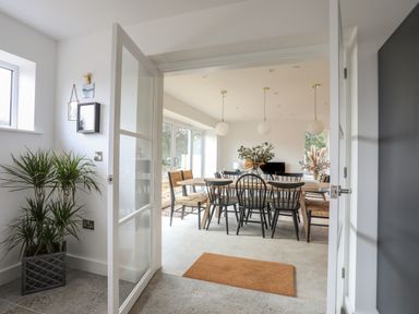 A dining room with a wooden table and black chairs viewed through open glass doors at Ysgol Fawr Big School in Benllech