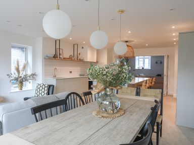 A dining area with a wooden table and chairs a kitchen in the background and a living area at Ysgol Fawr Big School in Benllech