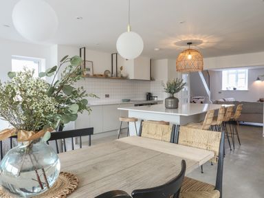 A kitchen and dining area with a wooden table chairs a kitchen island with bar stools and a vase with flowers at Ysgol Fawr Big School in Benllech