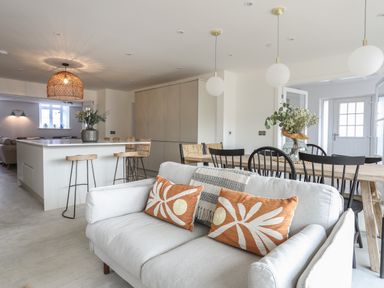 A kitchen and dining area with a light gray sofa and orange patterned cushions at Ysgol Fawr (Big School) in Benllech