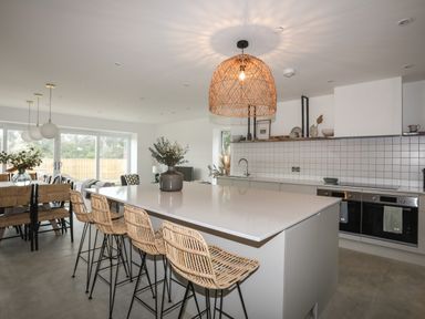 A kitchen with a large island with four bar stools and a dining area with chairs and a table with plants at Ysgol Fawr Big School in Benllech