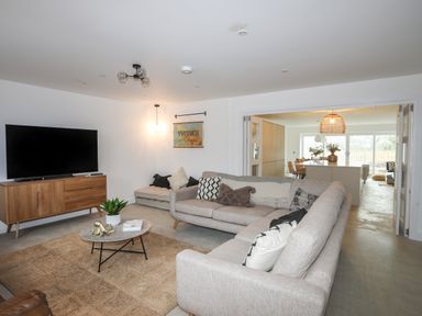 A living room with two sofas a coffee table a TV on a wooden stand and a visible kitchen in the background at Ysgol Fawr Big School in Benllech