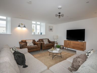 A living room with two brown armchairs two gray sofas a round coffee table and a wooden TV stand at Ysgol Fawr (Big School) in Benllech