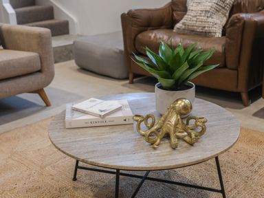 A living room with a round coffee table holding books a plant and a decorative octopus sculpture at Ysgol Fawr Big School in Benllech