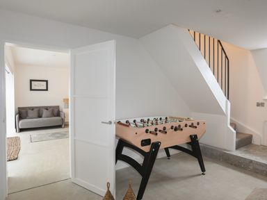 A foosball table in a room near a staircase with a door open to a living area with a sofa at Ysgol Fawr Big School in Benllech