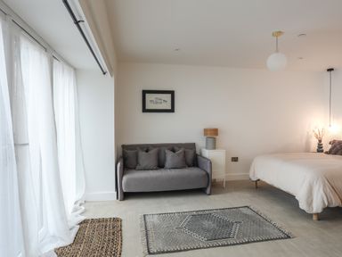 A bedroom with a grey sofa next to a bed and light curtains at Ysgol Fawr Big School in Benllech