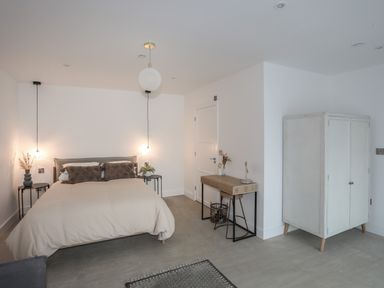 A bedroom with a bed bedside tables with lamps a wooden desk and a white wardrobe at Ysgol Fawr Big School in Benllech
