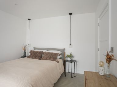 A bedroom with a bed and brown pillows with hanging pendant lights and side tables at Ysgol Fawr Big School in Benllech