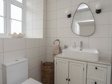 A bathroom with a toilet, a sink on a cabinet, a mirror, two wall lights, a towel on a ring, a wicker basket, and a window with a decorative shell at Ysgol Fawr Big School in Benllech