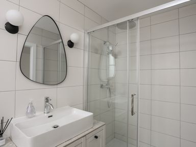 A bathroom with a rectangular sink a large mirror two wall lights and a glass shower enclosure at Ysgol Fawr Big School in Benllech