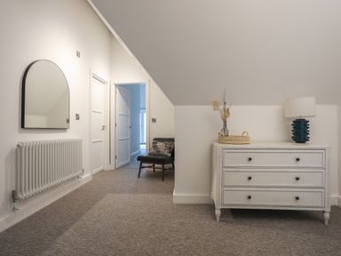 A hallway with a white dresser with a lamp and vase on top and a chair near two doors at Ysgol Fawr Big School in Benllech