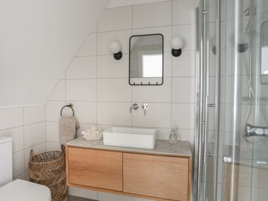 A bathroom with a wooden vanity and rectangular sink a mirror with lights towels and a shower at Ysgol Fawr Big School in Benllech