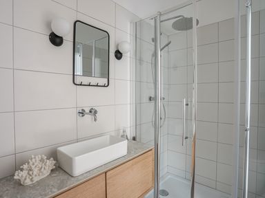 A bathroom with a rectangular sink on a wooden cabinet a mirror and two wall lights next to a glass shower at Ysgol Fawr Big School in Benllech