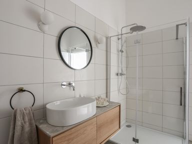 A bathroom with a round mirror above a sink on a wooden vanity next to a glass shower enclosure at Ysgol Fawr Big School in Benllech