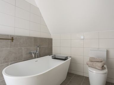 A bathroom with a bathtub, a toilet with towels on it, and tiled walls at Ysgol Fawr (Big School) in Benllech