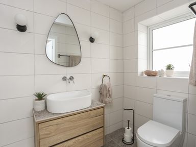 A bathroom with a wooden vanity and sink a teardrop mirror a toilet and a window with decor at Ysgol Fawr Big School in Benllech