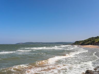 A beach with waves and people near cliffs and hills at Ysgol Fawr Big School in Benllech