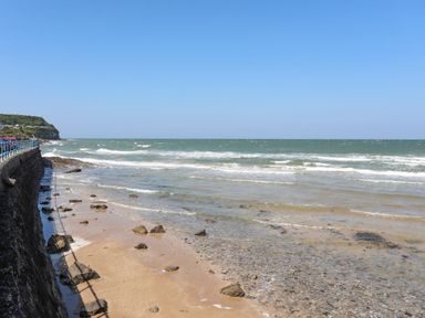 A rocky beach with waves and a stone seawall on the left at Ysgol Fawr Big School in Benllech